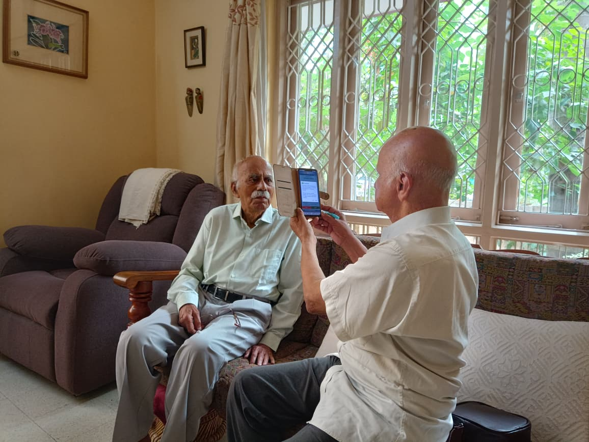 A volunteer helping a senior pensioner submit his Digital Life Certificate at home using a tablet